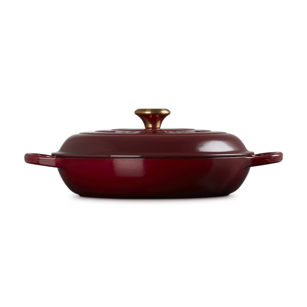 Casseruola rotonda in ceramica rossa con coperchio dorato, manici laterali e finitura lucida.