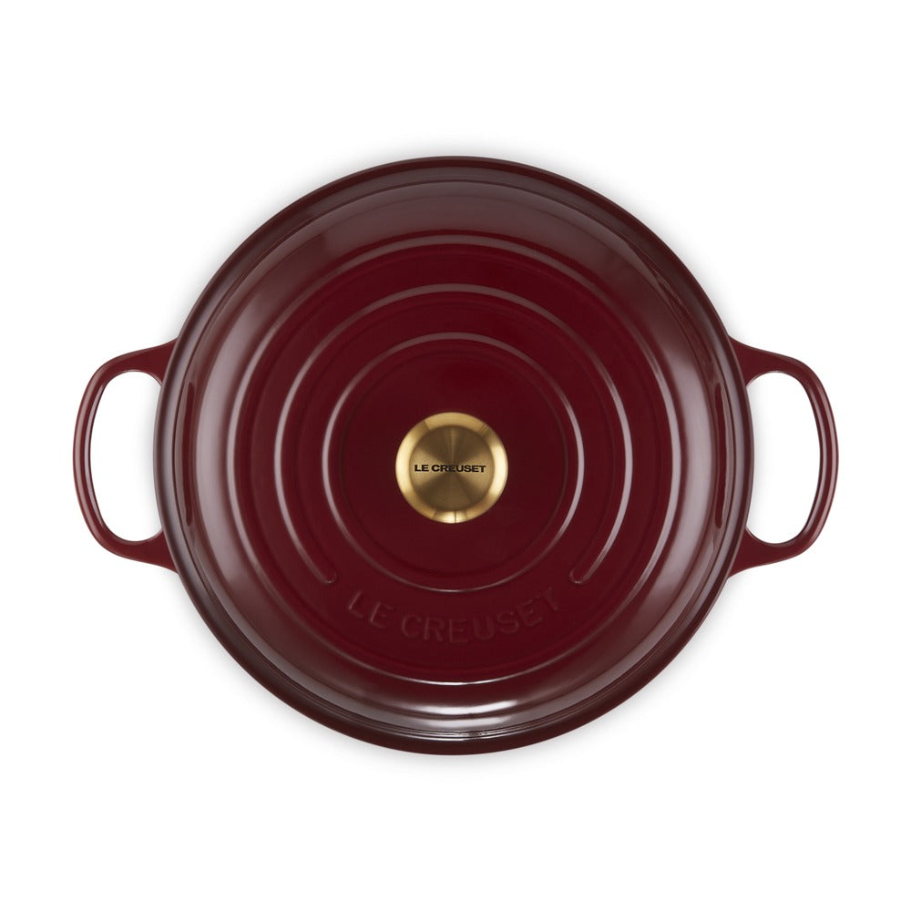 Casseruola rotonda di colore bordeaux con manici e fondo in metallo dorato, marchiata "LE CREUSET".