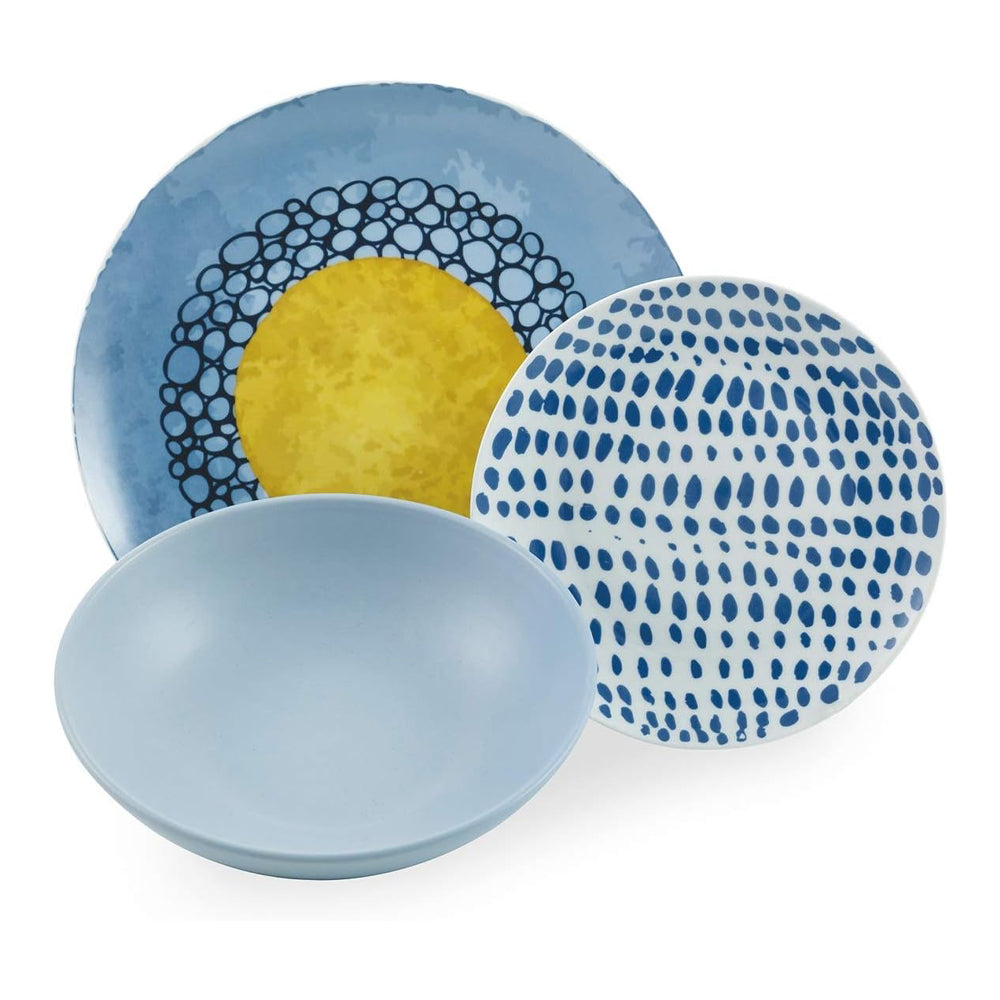Trois assiettes en céramique : une bleue avec cercles noirs et soleil jaune, une bleu clair avec motifs goutte et une assiette creuse bleu pastel.