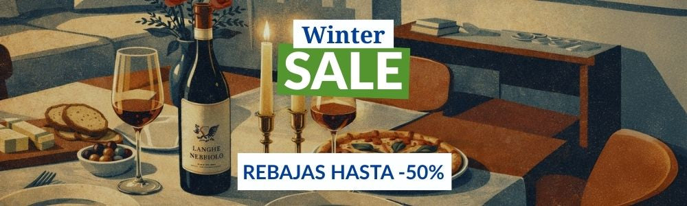Bottiglia di vino rosso Langhe Nebbiolo, calici con vino, pane, ciotola di olive, pizza e due candele accese su tavolo rotondo in arredamento moderno.