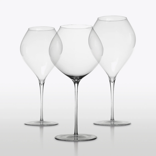 Trois calices transparents en verre à pied fin et large corolle évasée sur fond clair uniforme
