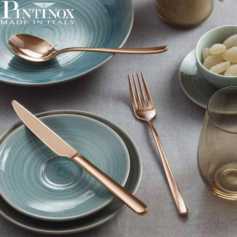 Cubiertos de metal color oro rosa con platos turquesa esmaltados sobre mantel gris, logo Pintinox Made in Italy