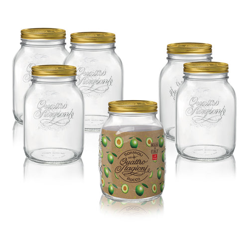 Fünf transparente Glasgefäße mit goldenen Deckeln, eines vorne mit Etikett mit grünen Oliven und Aufschriften "Quattro Stagioni" und "Made in