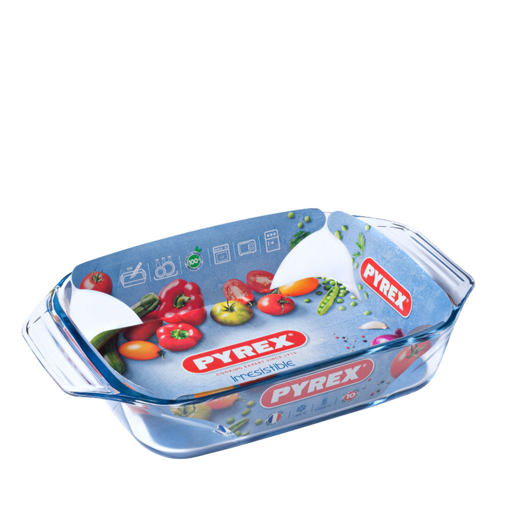 Plat à four rectangulaire transparent en verre avec poignées latérales et étiquette bleue avec logo rouge Pyrex et images de légumes.