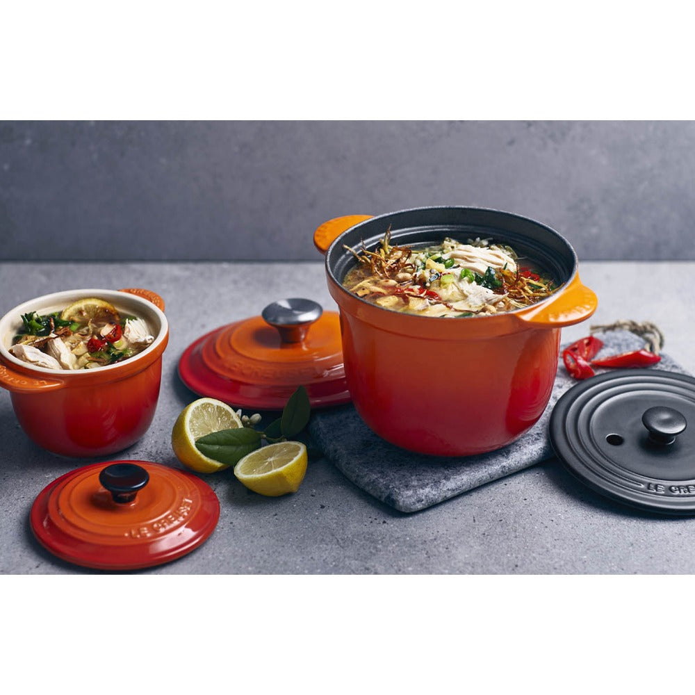 Casseroles en fonte orange avec nourriture, citron frais et torchon gris. En arrière-plan, surface grise lisse.