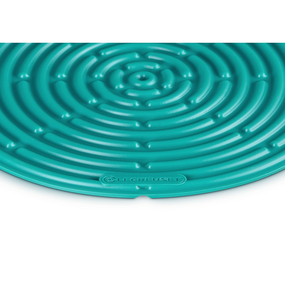 Tapis circulaire en silicone turquoise à motif spiralé, logo "LE CREUSET" en bas.