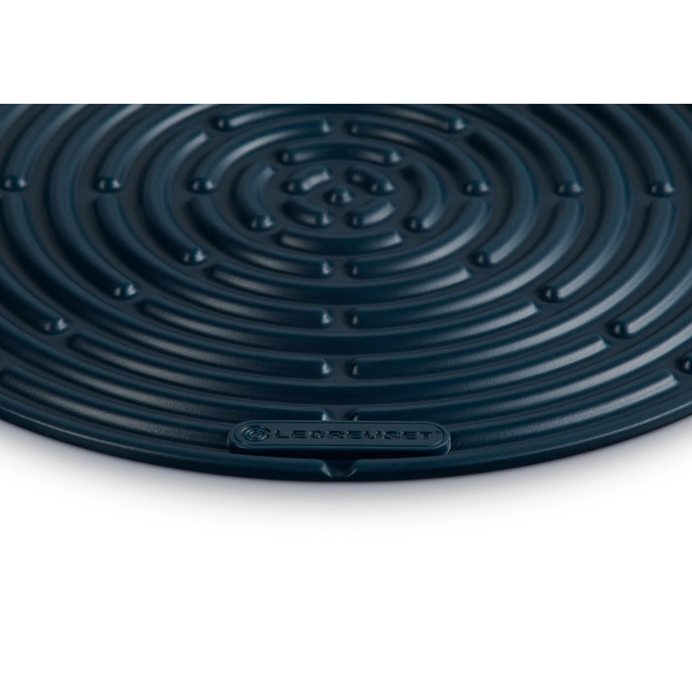 Tapis circulaire en plastique bleu foncé à motif spiralé et surface ondulée, marqué "Le Creuset".