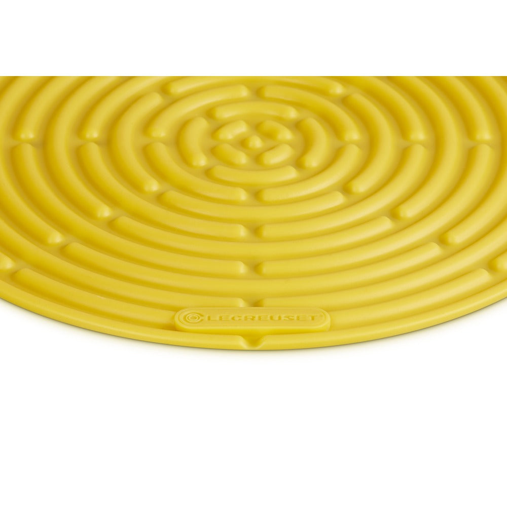 Tapis circulaire jaune en silicone à motif spiralé, portant la marque "Le Creuset" en relief.