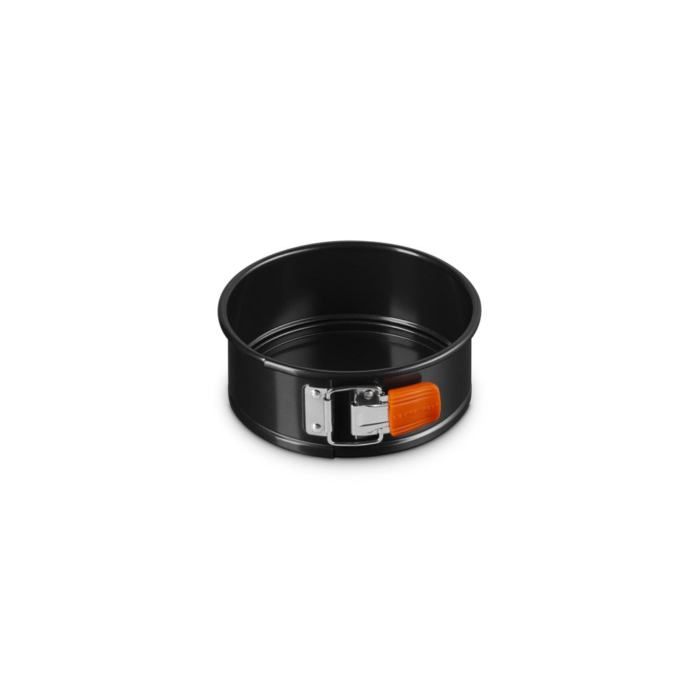 Moule à gâteau rond, noir, avec fermeture métallique et joint orange. Surface lisse et brillante.