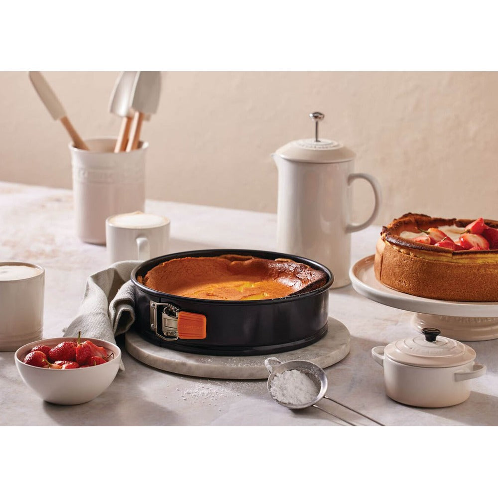 Gâteau dans moule noir avec bord, bol blanc de fraises, lait en tasse, sucre, cadre lumineux et minimaliste.