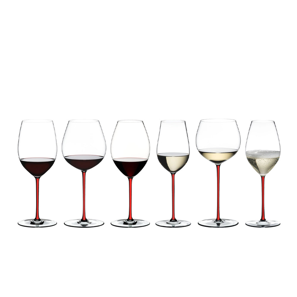 Seis copas de vidrio transparente con tallo rojo, con vino tinto, blanco y espumoso, alineadas sobre fondo blanco.