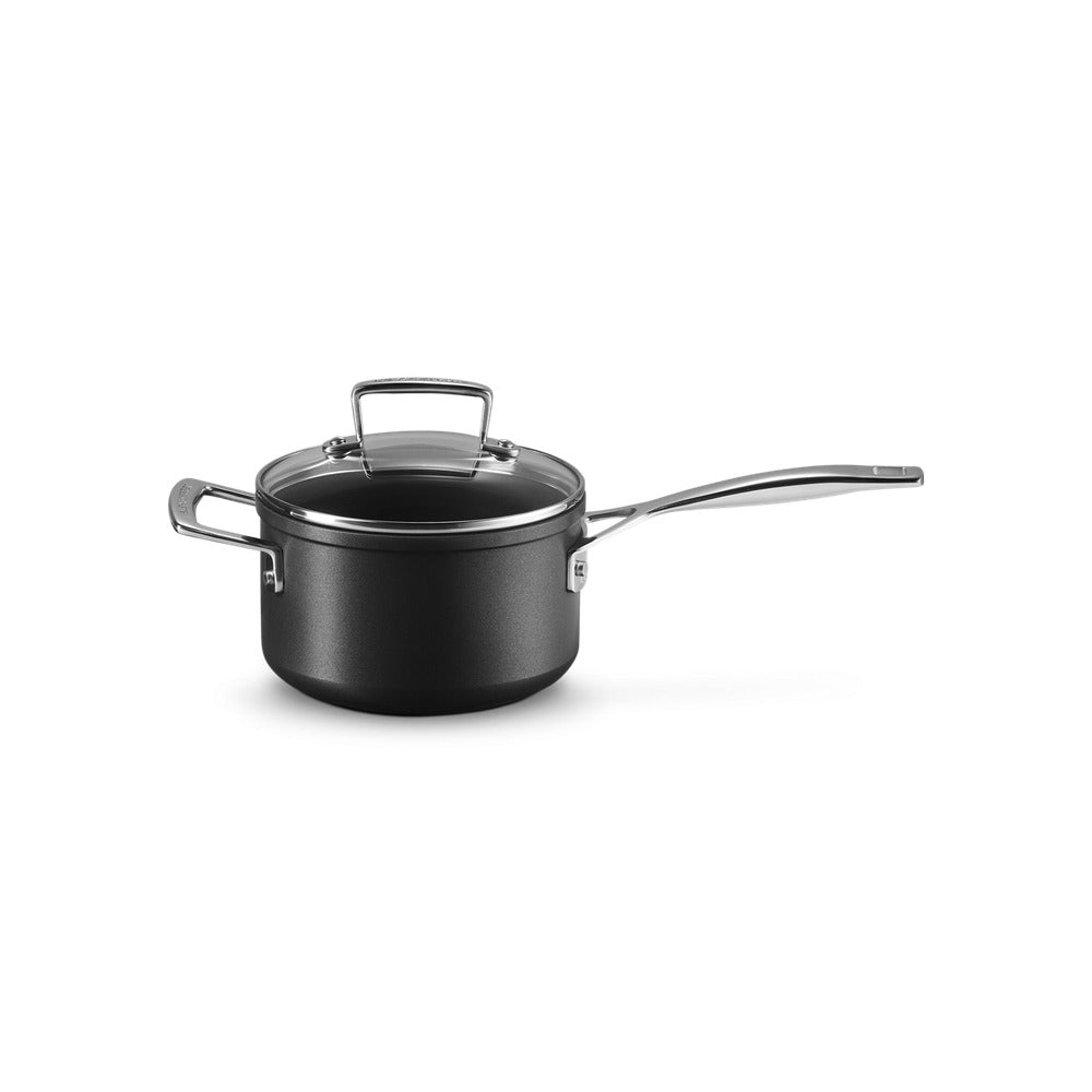 Pentola nera con coperchio trasparente, manico lungo in acciaio inox, superficie liscia e rotonda, posizionata su sfondo bianco.