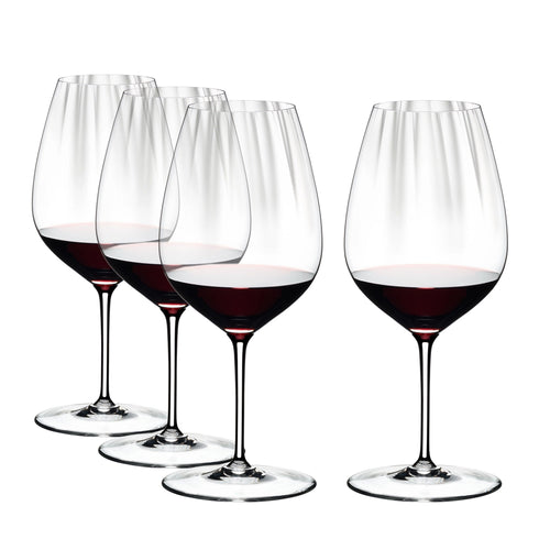quattro bicchieri in vetro trasparente con vino rosso versato fino a un terzo, sfondo bianco