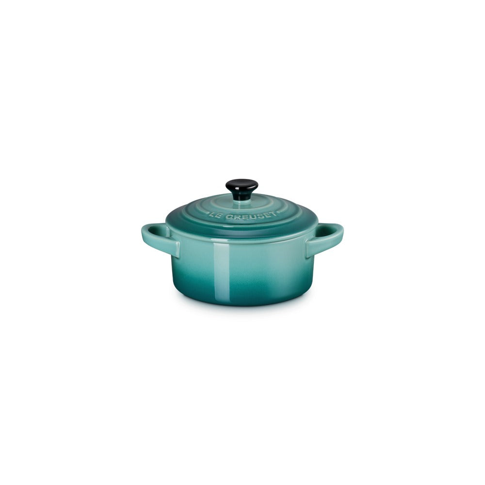 Casseruola in ceramica smaltata verde acqua con coperchio nero e manici, posizionata su sfondo neutro.