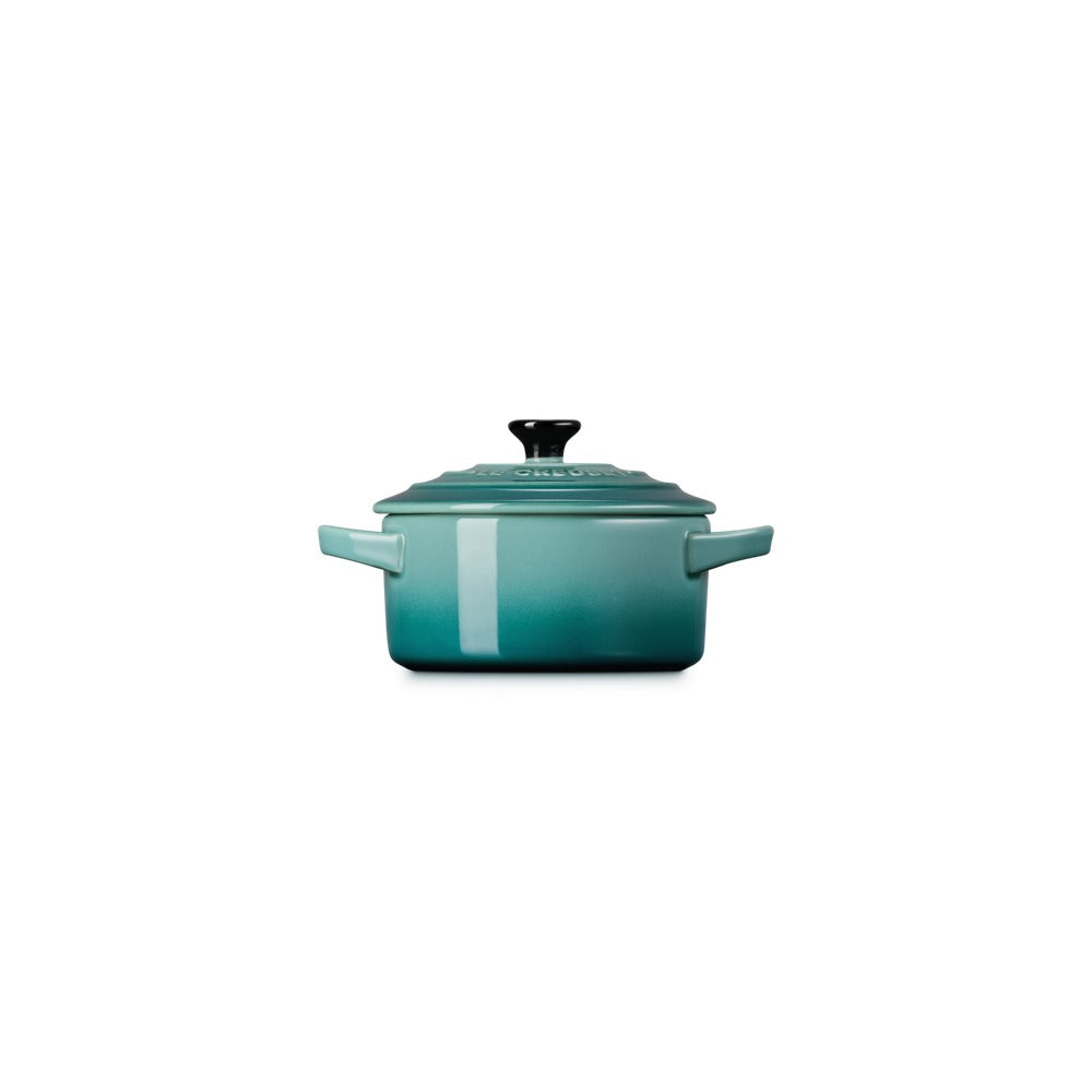 Casseruola in ceramica verde acqua con coperchio e manici, superficie liscia e lucida, presentata su sfondo bianco.