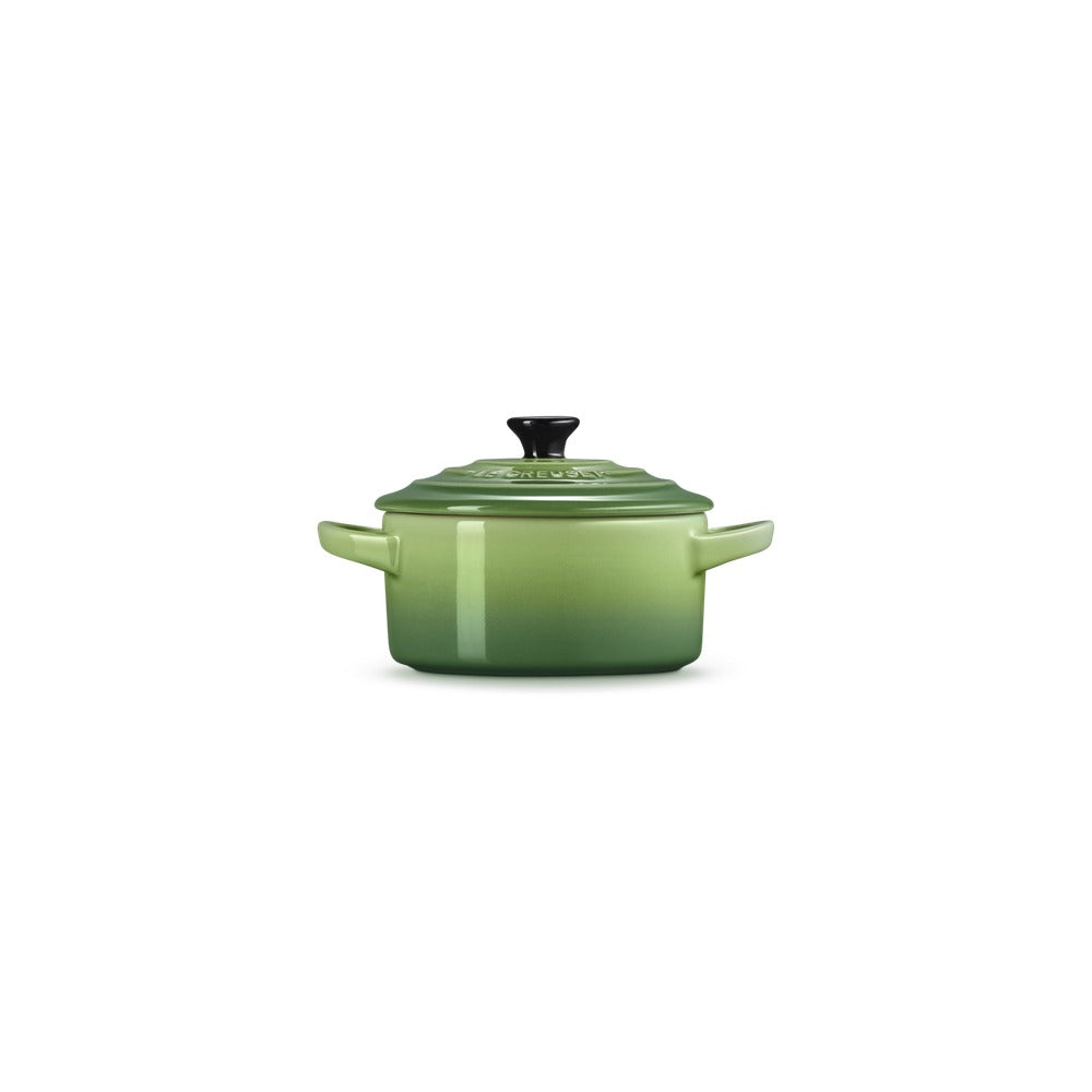 Casseruola verde in porcellana con coperchio nero, impugnature laterali, superficie lucida e sfumature di colore.