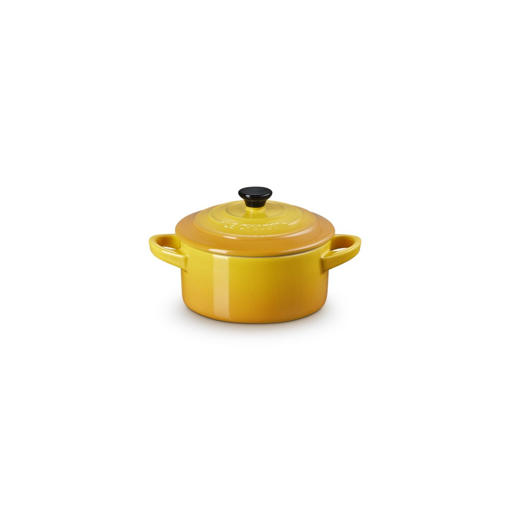 Casseruola rotonda di ceramica gialla con manici e coperchio nero. Design lucido e semplice, su sfondo bianco.