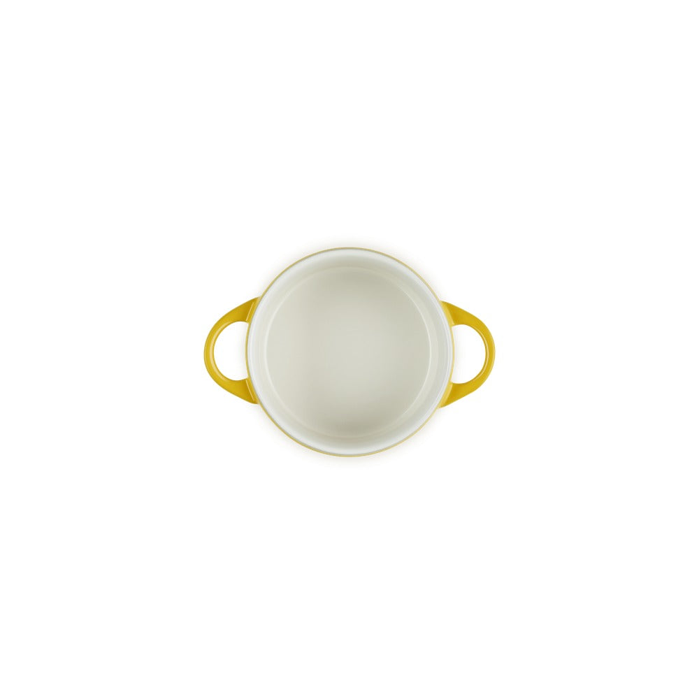 Casseruola bianca con manici gialli, di forma rotonda e materiale ceramico, vista dall'alto su fondo bianco.