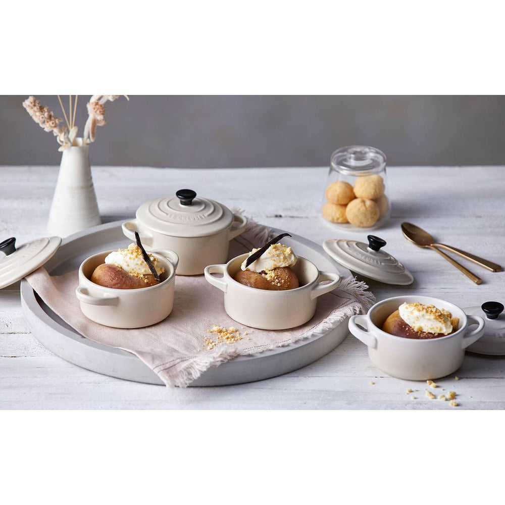 Ciotole di ceramica beige con dessert, panna e vaniglia, su un vassoio grigio e tovagliolo beige; al lato biscotti in barattolo.