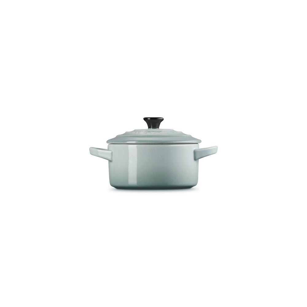 Casseruola di colore verde chiaro con coperchio nero, forma rotonda e manici laterali. Sfondo bianco.