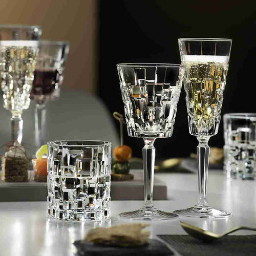 Set transparenter Gläser mit geometrischen Mustern, bestehend aus Weingläsern und Tumblern auf Tisch mit dunklem Hintergrund und unscharfen Antipasti.