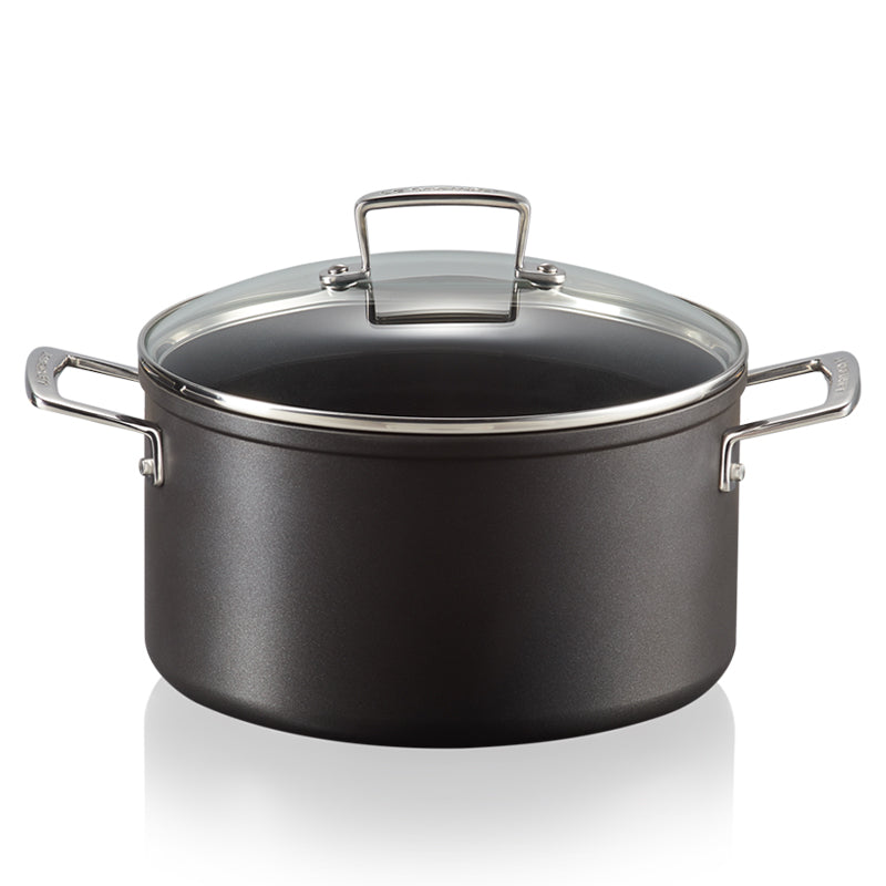 Olla alta negra con tapa transparente y asas de metal brillante. Superficie ligeramente mate, colocada sobre fondo blanco reflectante.