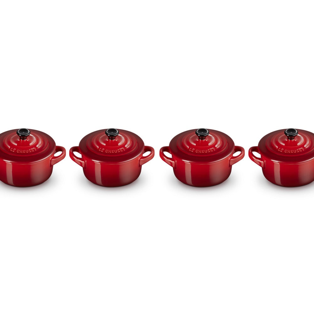 Set di quattro cocotte rotonde rosse con manici e coperchio nero, su sfondo bianco.