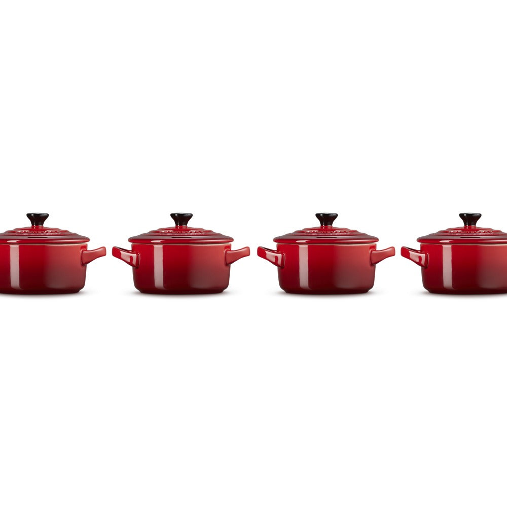 Quatre casseroles rouges en fonte, avec couvercle et poignées, alignées sur un fond blanc.