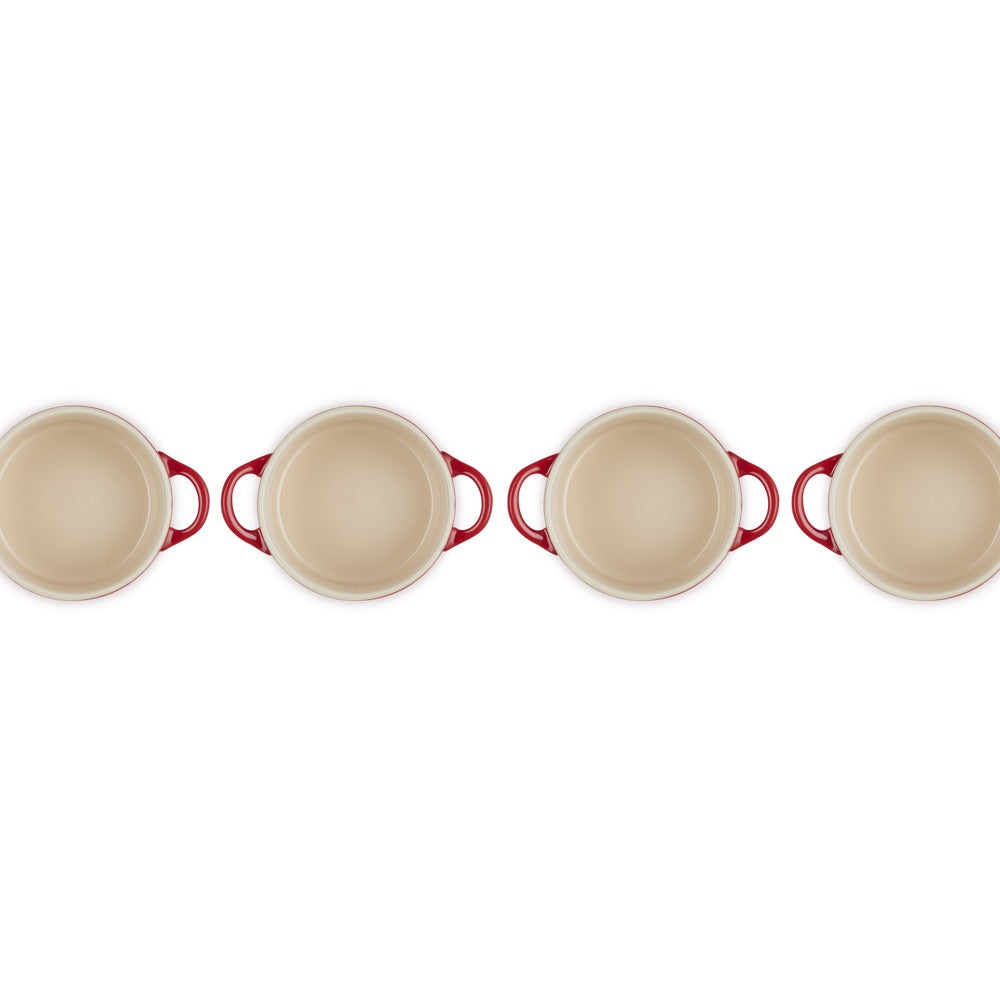 Quatre casseroles rondes avec poignées rouges, beige à l'intérieur, disposées en rangée sur fond blanc.