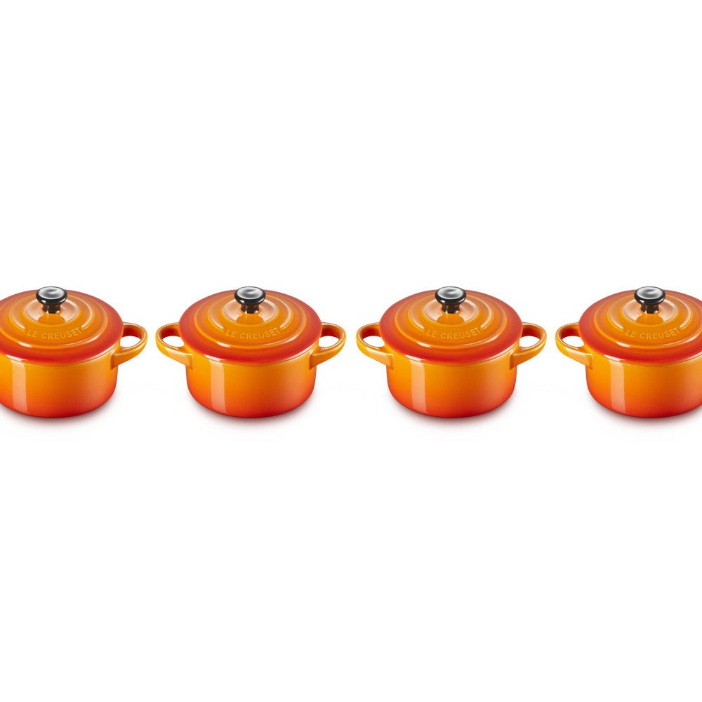 Set di quattro cocotte in ceramica arancione, con coperchio e manico, disposte in fila su fondo bianco.
