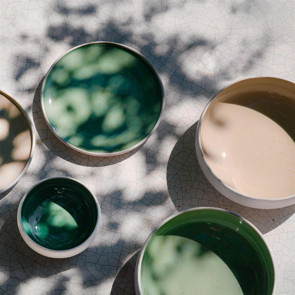 ciotole in ceramica di varie dimensioni con interni verdi e beige su superficie chiara screpolata con ombre di foglie sopra