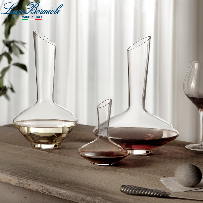 Tre decanter in vetro trasparente di forme storte con vino rosso e bianco su tavolo in legno chiaro