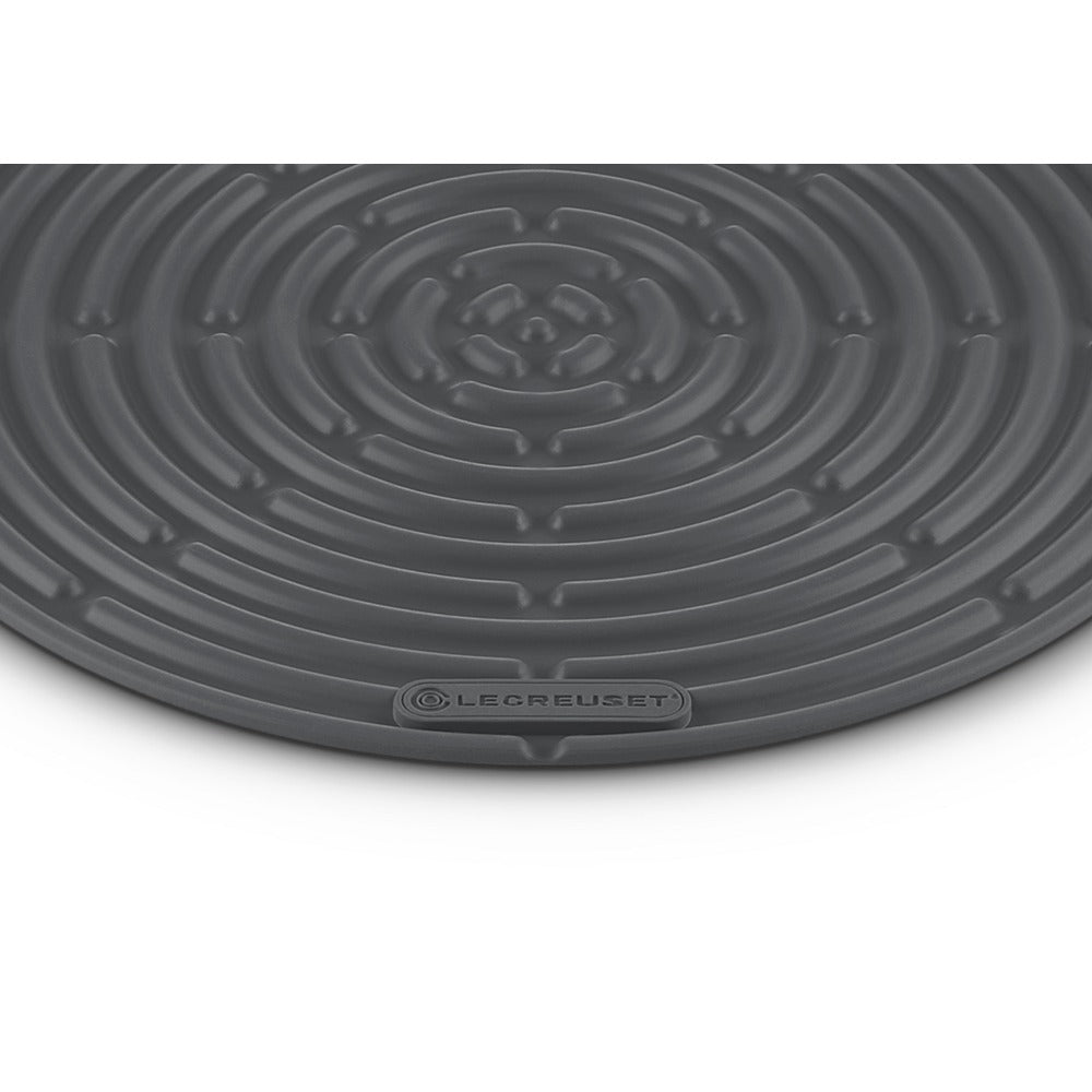 Tapis rond gris foncé à motif spiralé et logo "LE CREUSET" en bas.