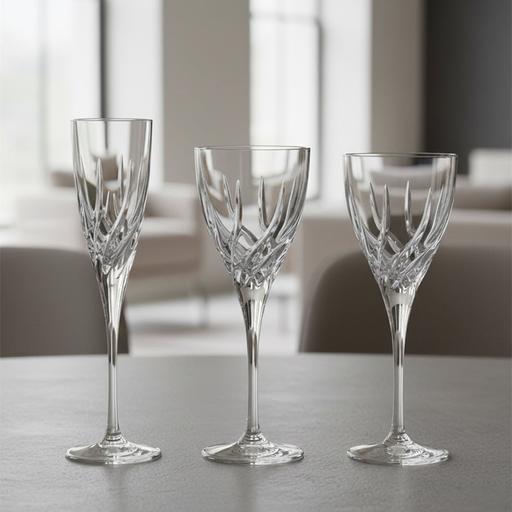 Tre calici di cristallo trasparente con incisioni decorate, posati su una superficie grigia in ambiente interno sfocato e luminoso.