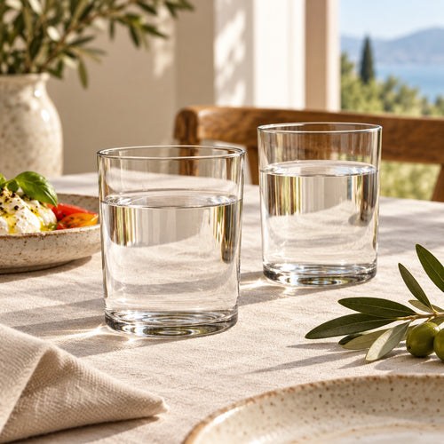 bicchiere trasparente cilindrico di vetro contenente acqua, su sfondo bianco uniforme