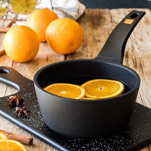 Casserole noire avec tranches d'orange dans un liquide sombre, sur planche en bois à côté d'oranges entières.