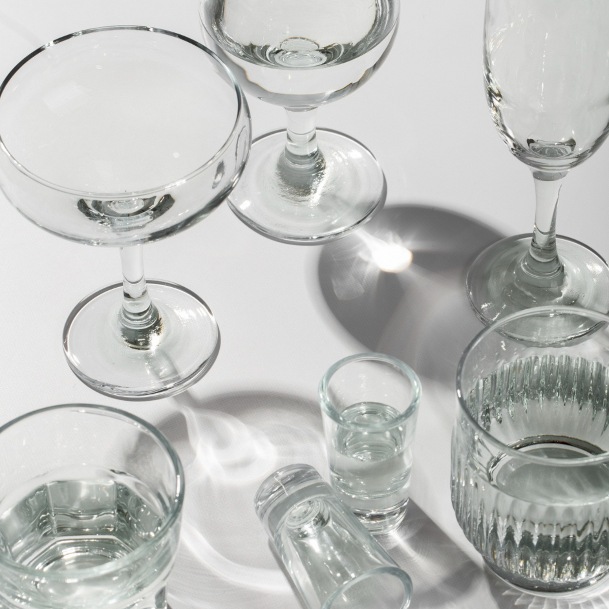 Set of eight transparent glass cups in various shapes and sizes on white background, with light reflections.