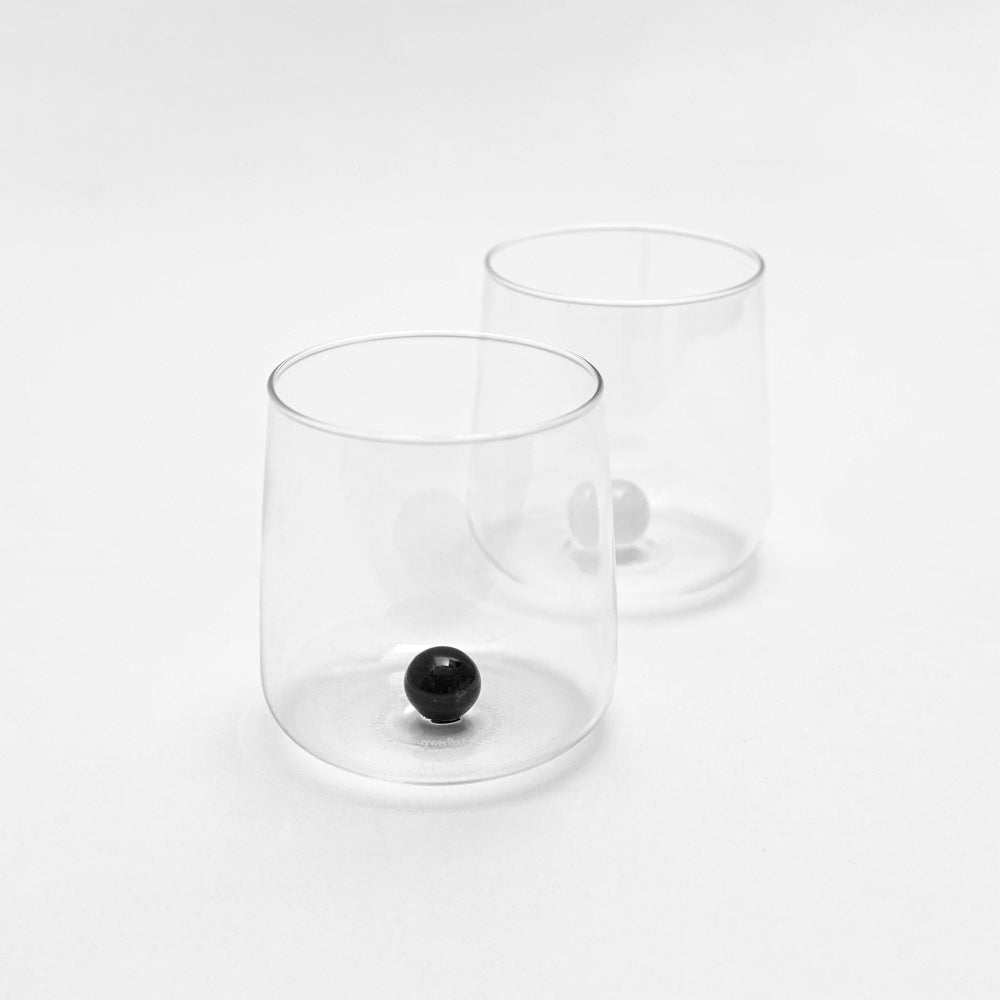 Twee transparante glazen of plastic glazen met interne bolvormige basis, een met zwarte bol en de andere met lichte bol, op witte achtergrond.