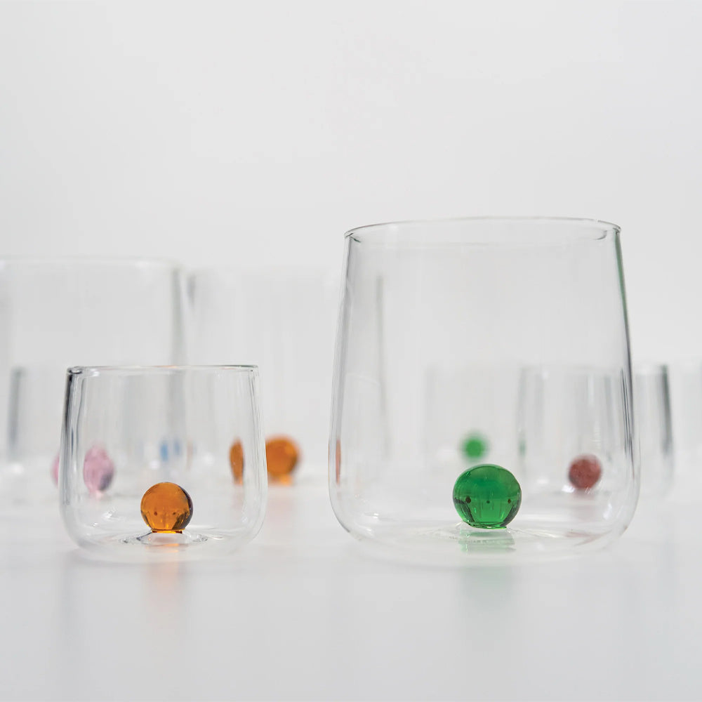 Transparante glazen met gekleurde oranje, groene, roze en blauwe balletjes erin op wit oppervlak