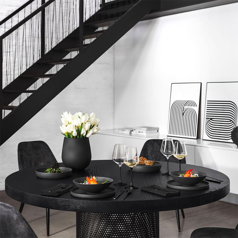 Table ronde noire en bois avec vase noir mat et tulipes blanches, assiettes et verres à vin, sous escalier intérieur métallique noir.