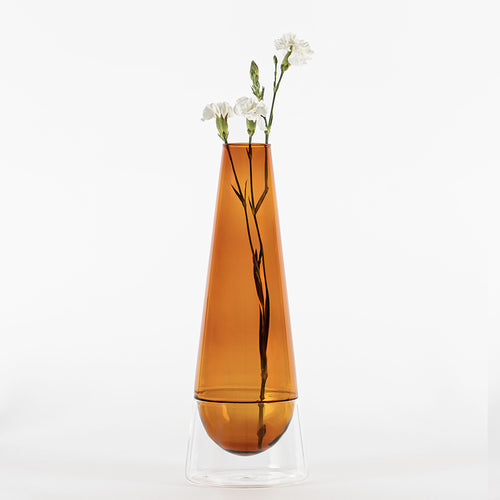 vaso di vetro trasparente color ambra con base trasparente contenente tre fiori bianchi e verdi su sfondo bianco