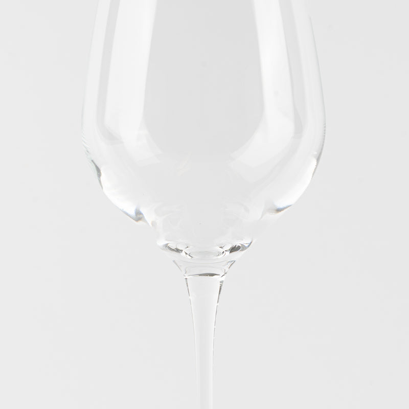 Calice à vin transparent en verre avec long pied sur fond blanc uniforme.