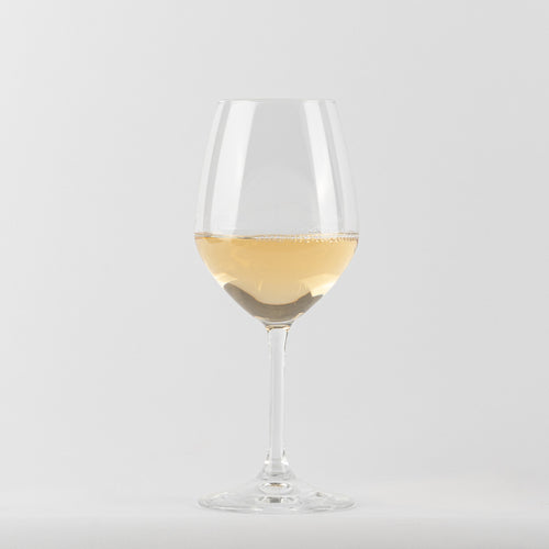 Verre à vin en verre transparent contenant un liquide jaune clair avec bulles, fond blanc.
