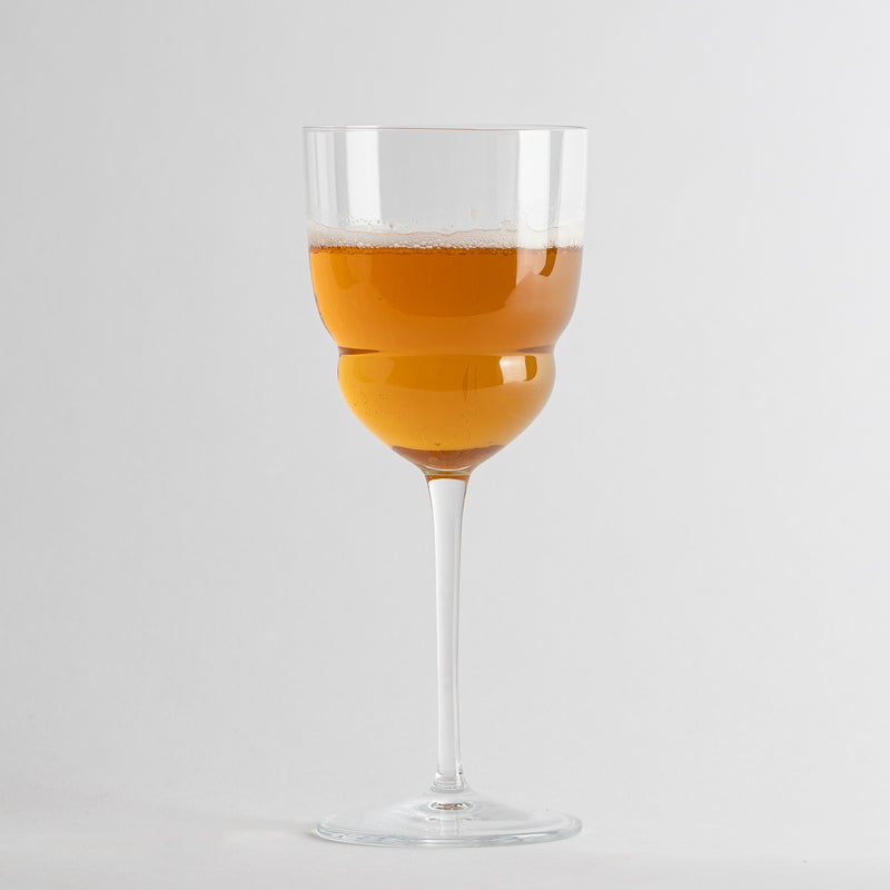 Transparentes Glas-Weinglas mit langem Stiel, gefüllt mit schaumigem orangefarbenem Getränk auf weißem Hintergrund