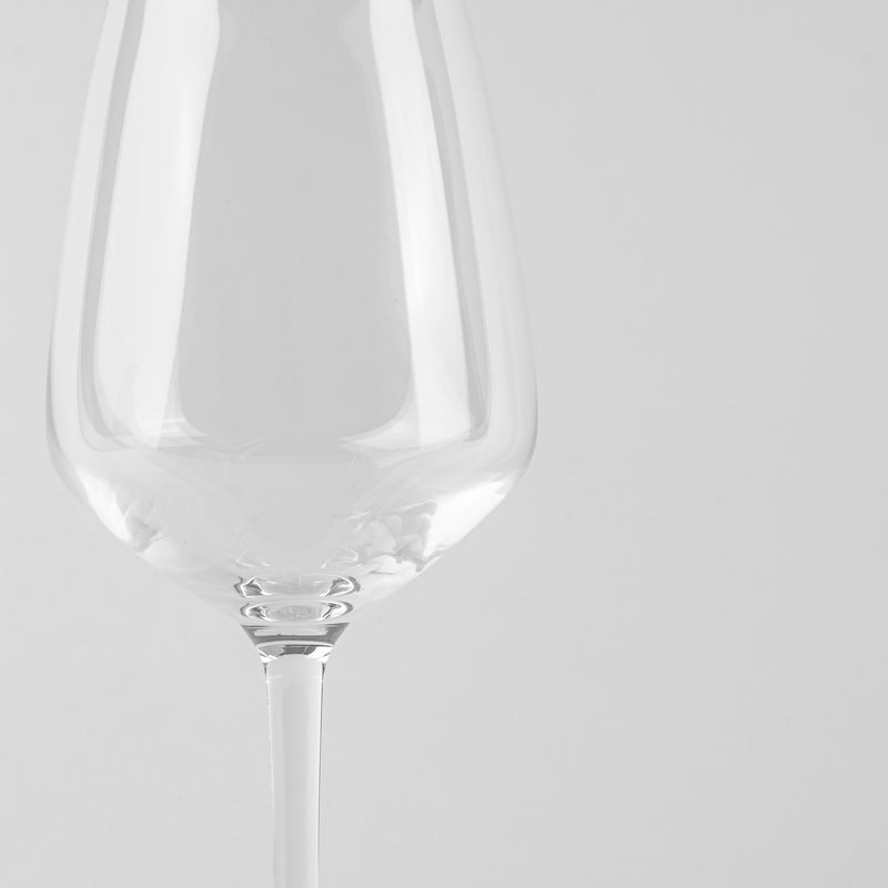 Copa de vino de vidrio transparente de forma ancha con tallo fino sobre fondo gris uniforme.
