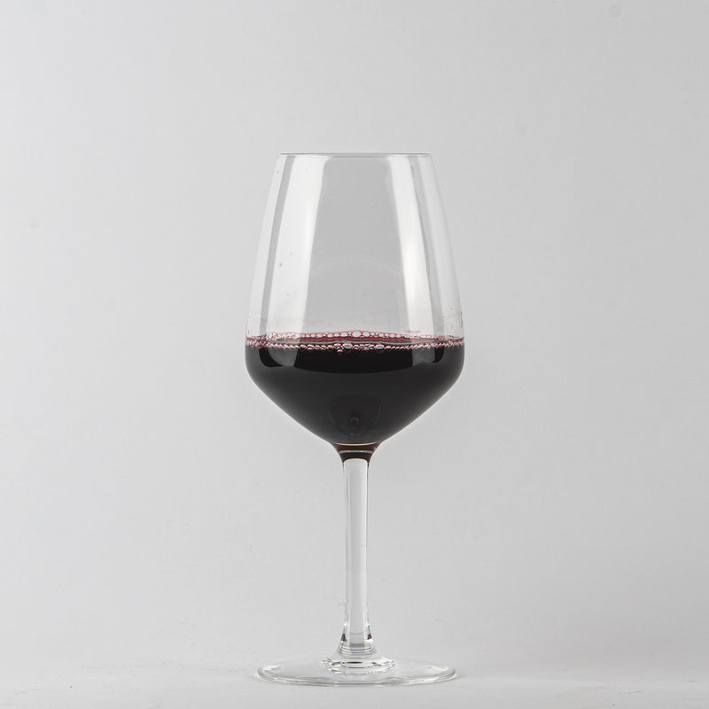 Copa de vino de vidrio transparente con vino tinto y burbujas sobre fondo gris claro