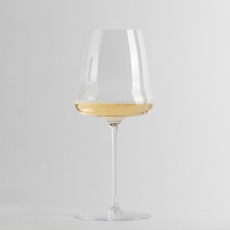 Transparent glass wine glass with long stem containing lightly sparkling white wine on grey background