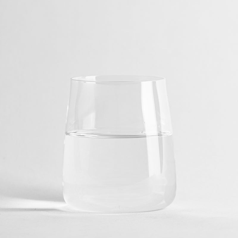 Transparante glazen beker met acqua halfvol op uniform witte achtergropd