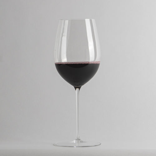 calice di vetro trasparente a stelo con vino rosso fino a metà sfondo grigio chiaro uniforme