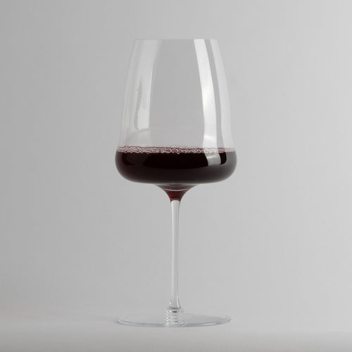 Calice trasparente in vetro con vino rosso all'interno su sfondo grigio chiaro.